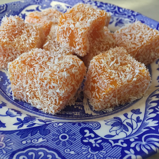 Photo of orange squares on a plate covered in desiccated white coconut placed on a blue and white china spode plate